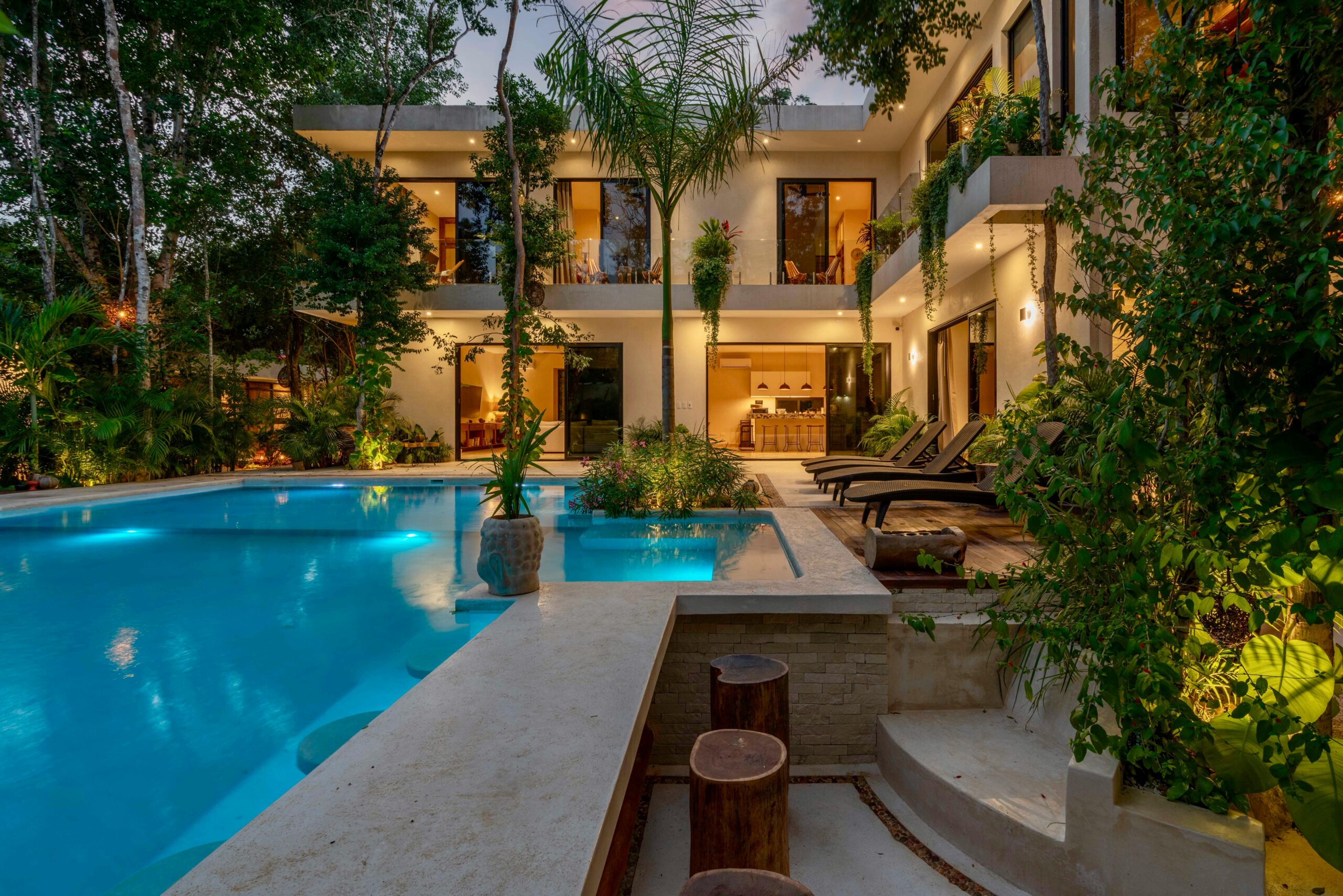 Modern luxury villa with a lit pool and tropical garden. Evening view.