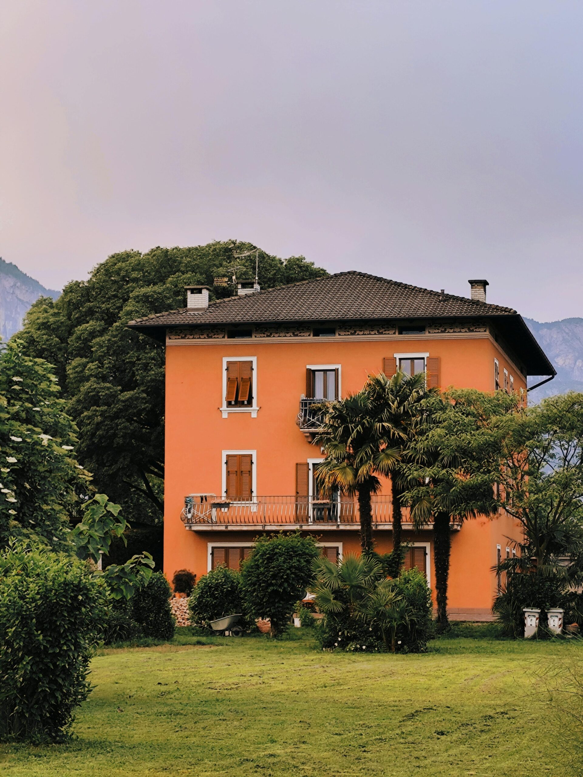 A picturesque orange villa surrounded by greenery and mountains in Italy.
