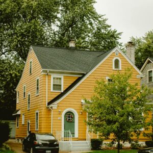 A charming yellow two-story house with a green door, car parked outside.